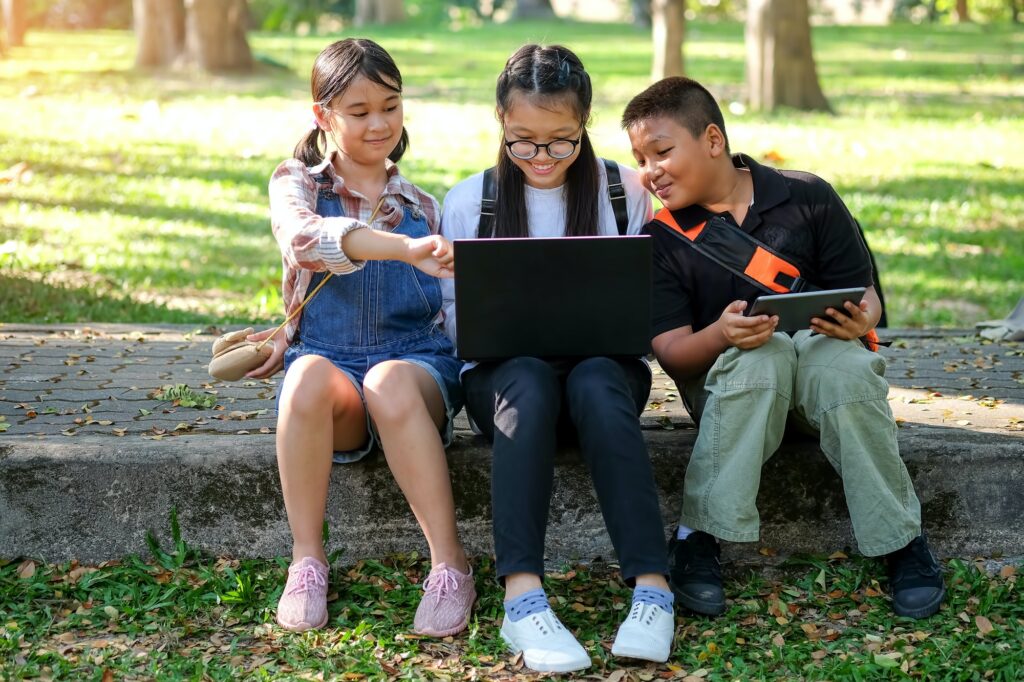 asian children are playing laptop computer in the park