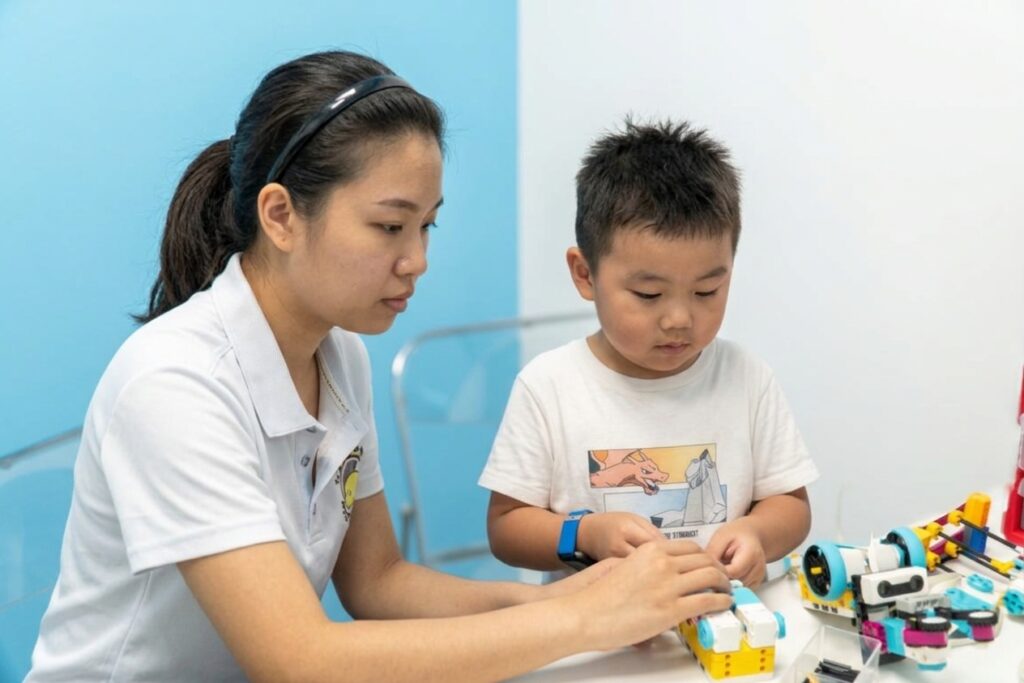 A trainer guiding a child as they build with LEGO robotics components.