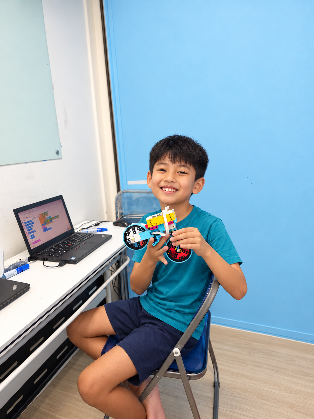 AI-edited illustration of a child holding a robotics project beside a coding laptop